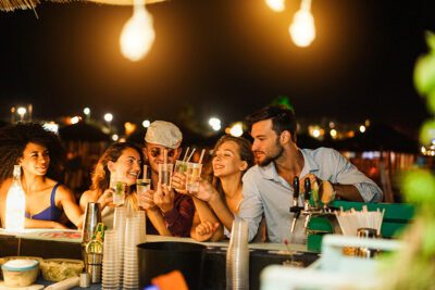 Happy friends cheering and drinking cocktails at beach party outdoor - Soft focus on right man face