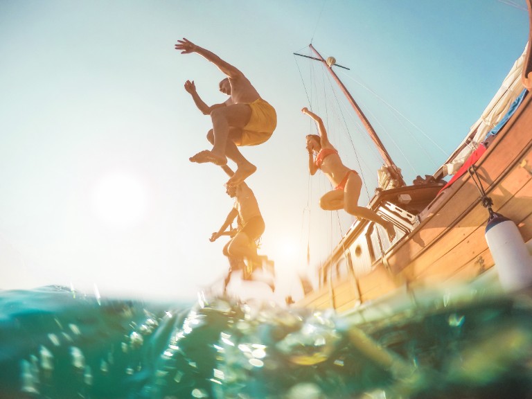 Happy friends diving from sailing boat